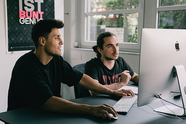 Zwei Männer arbeiten gemeinsam an einem iMac