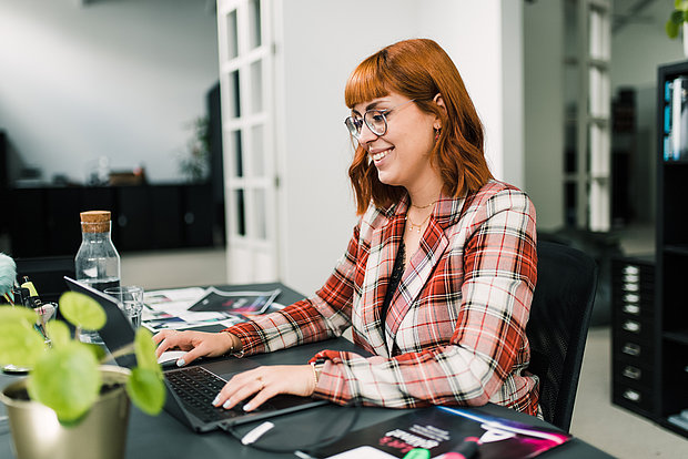 Lächelnde Designerin sitzt vor einem Laptop und arbeitet