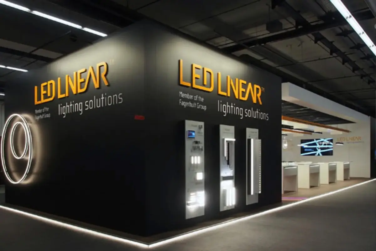 Messestand von LED Linear mit beleuchtetem Logo, kreisförmigem Lichtobjekt und Vitrinen mit Leuchtenexponaten auf der Messe Light & Building.