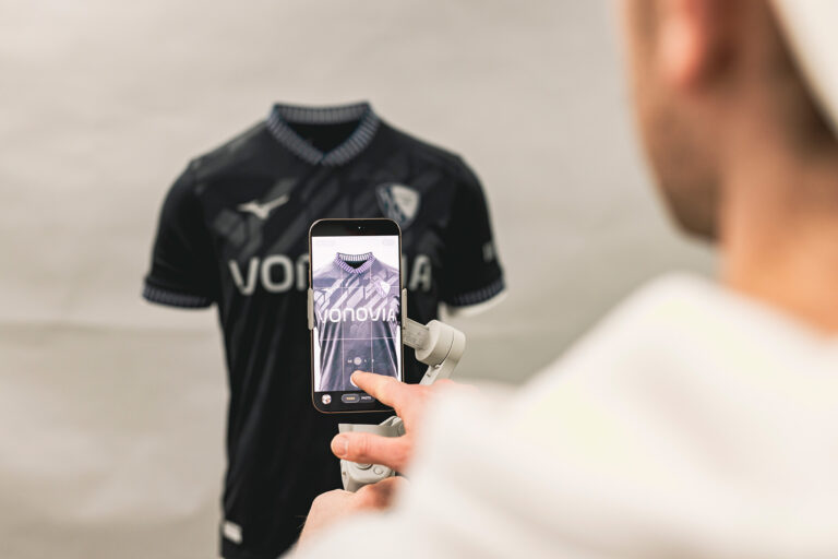 Fotograf nimmt Trikot mit Vonovia-Sponsoring für Social-Media-Content mit dem Smartphone auf