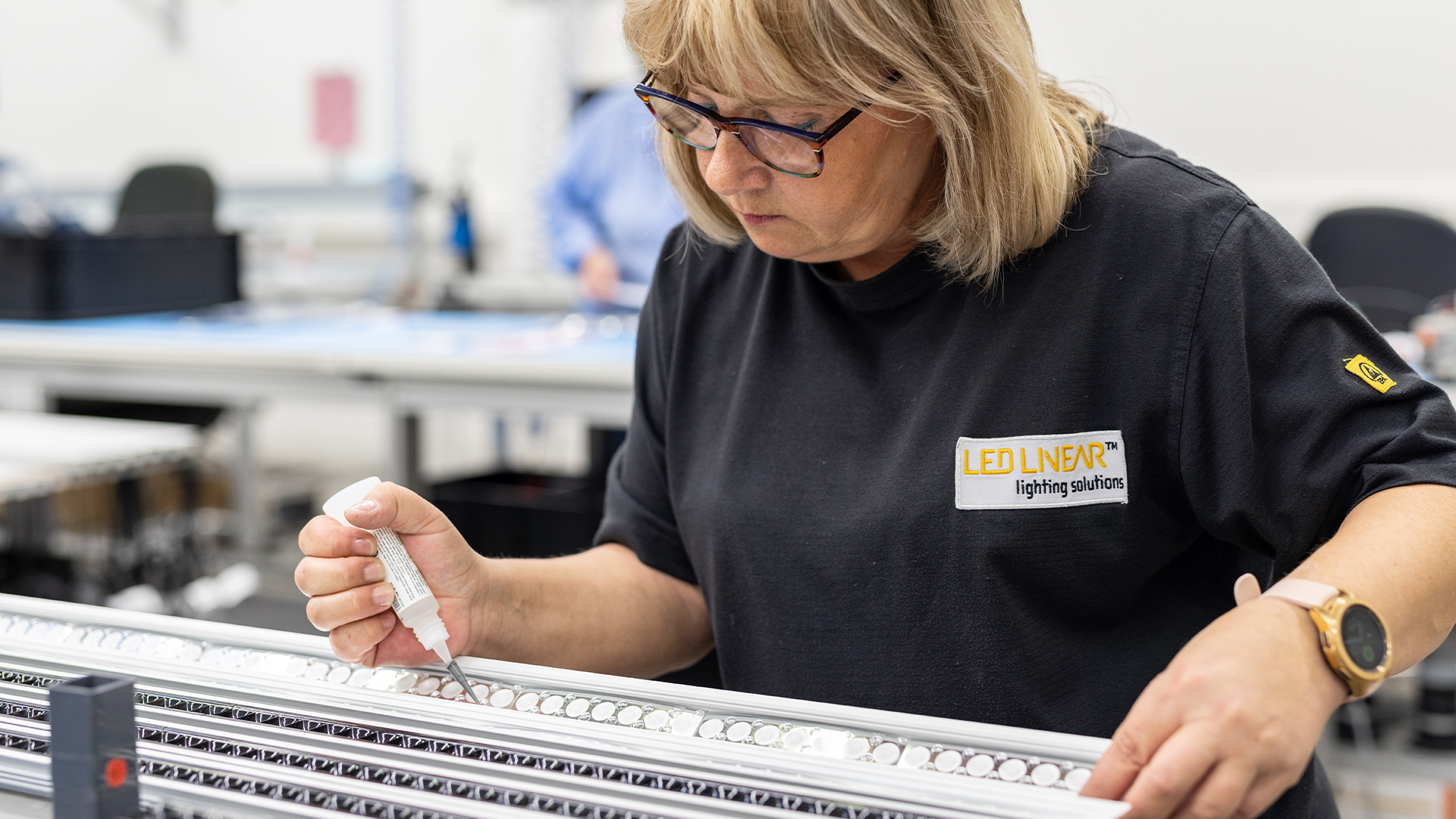 Mitarbeiterin von LED Linear arbeitet mit einer Dosierflasche präzise an einem LED-Profil mit Linsen