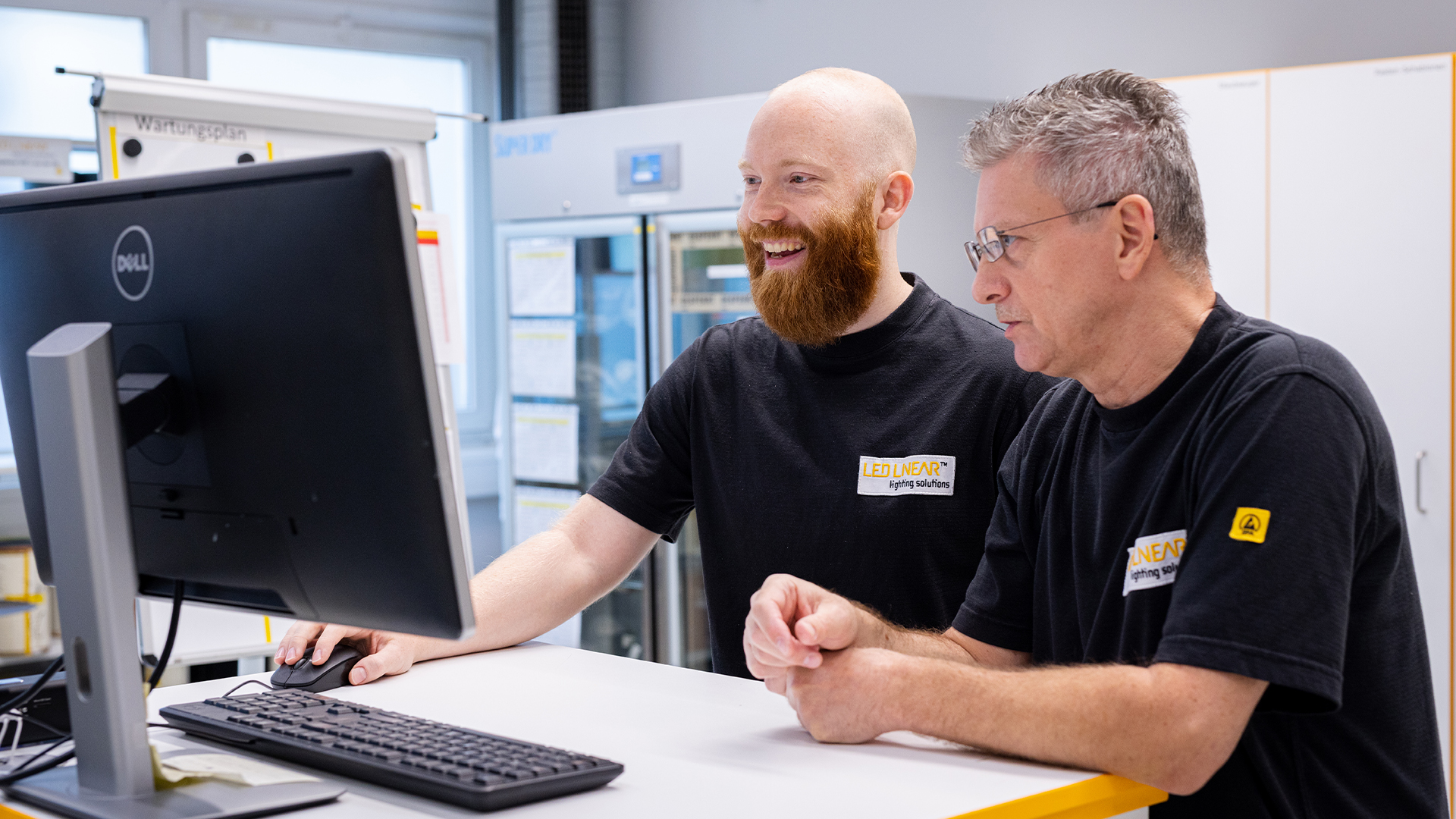 Zwei Mitarbeiter von LED Linear besprechen sich gut gelaunt vor einem Monitor