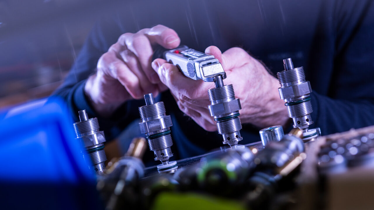 Hände montieren mit einem Werkzeug Hydraulikventile aus Edelstahl an einem Arbeitsplatz