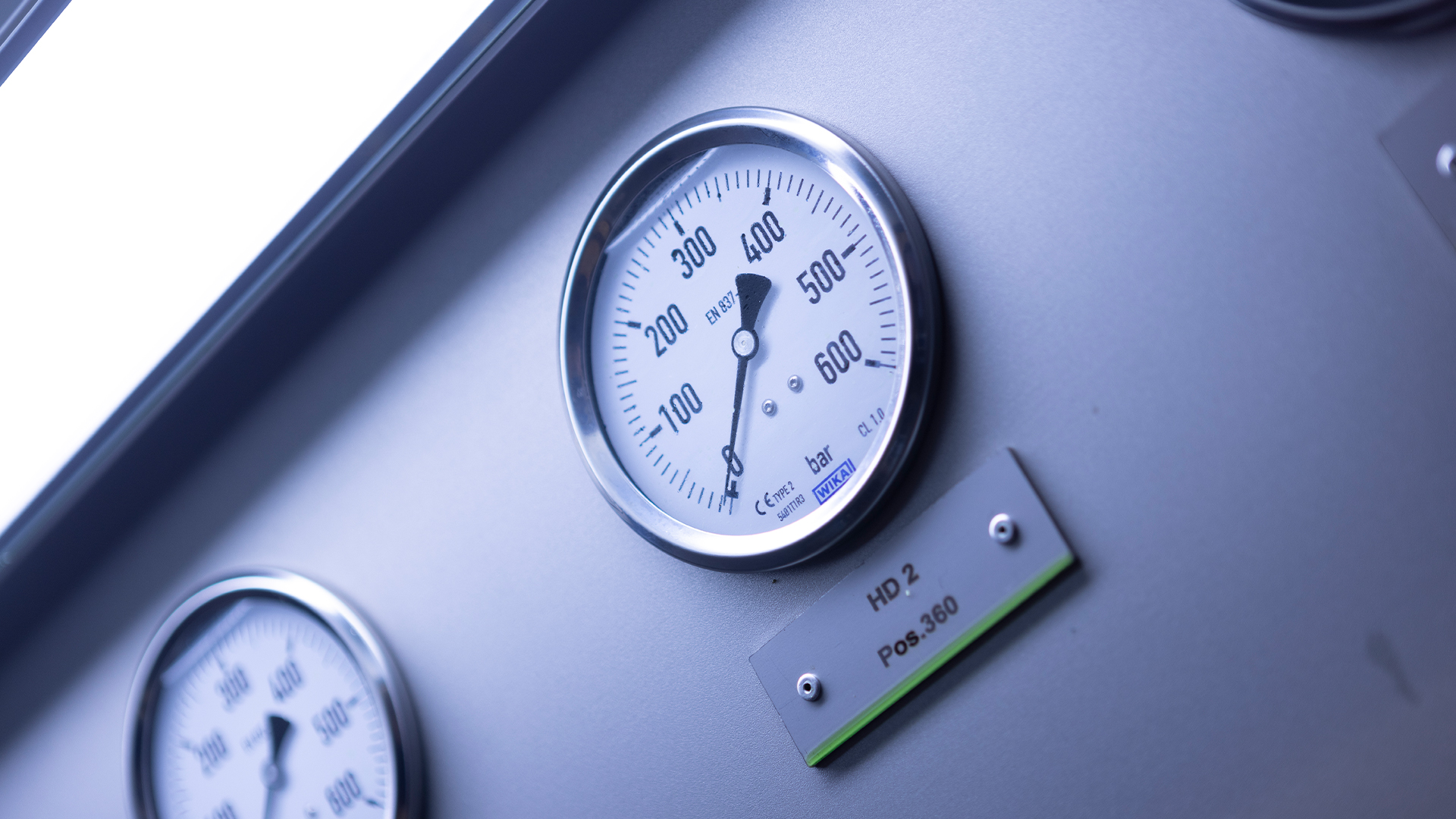 Manometer mit Skala bis 600 bar an einer grauen Prüfwand, darunter ein zweites Manometer