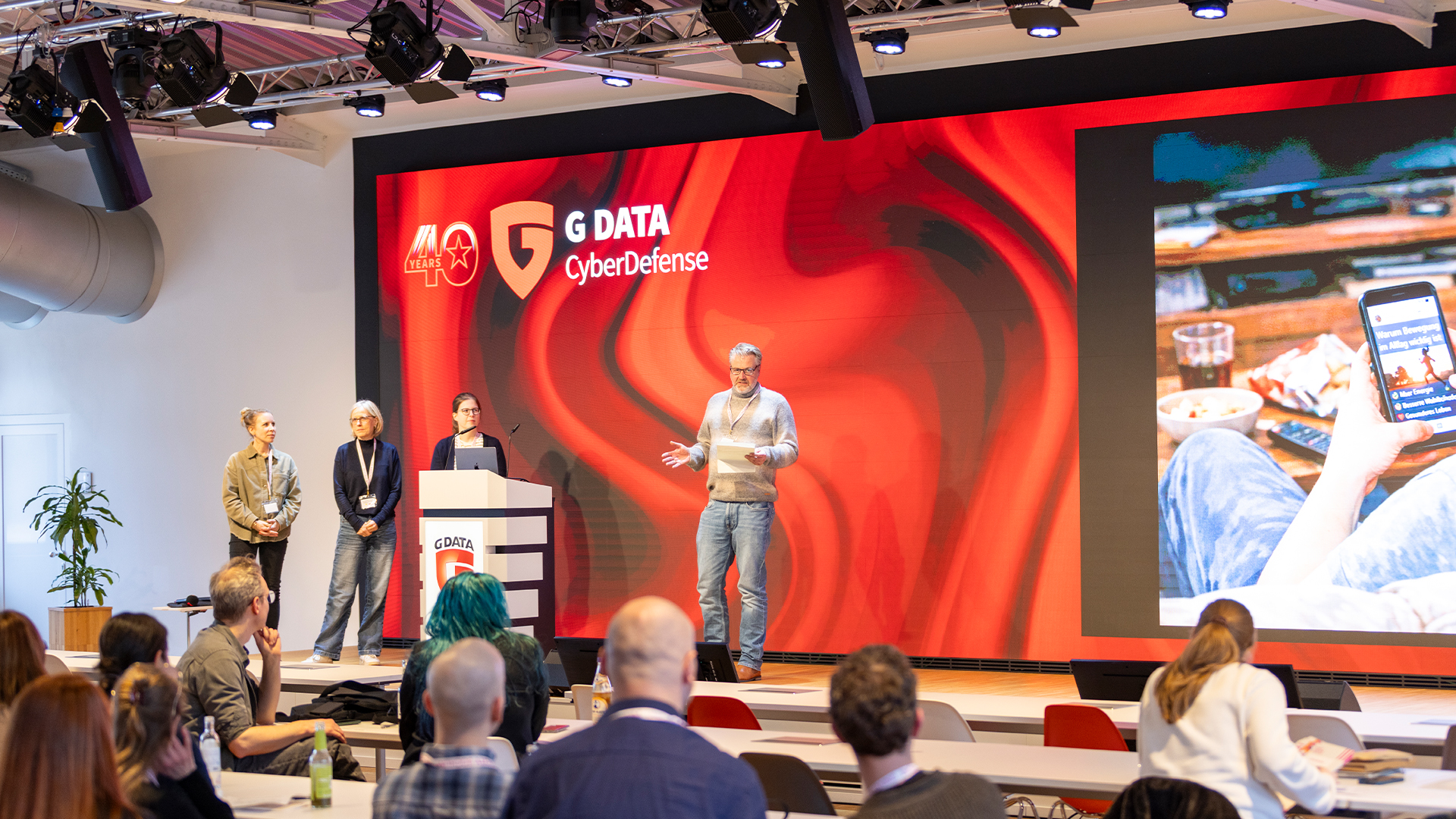 Vier Personen auf der Bühne vor einer G DATA LED-Wand, im Vordergrund das Publikum