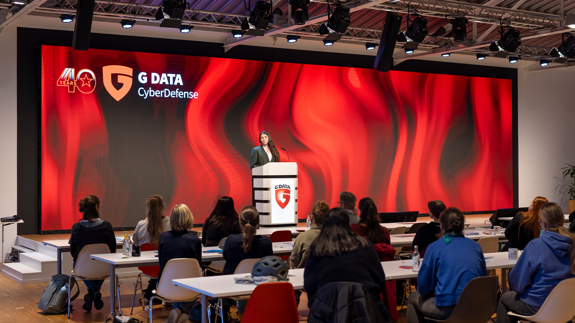 Rednerin am G DATA Rednerpult vor roter LED-Wand, im Vordergrund das Publikum