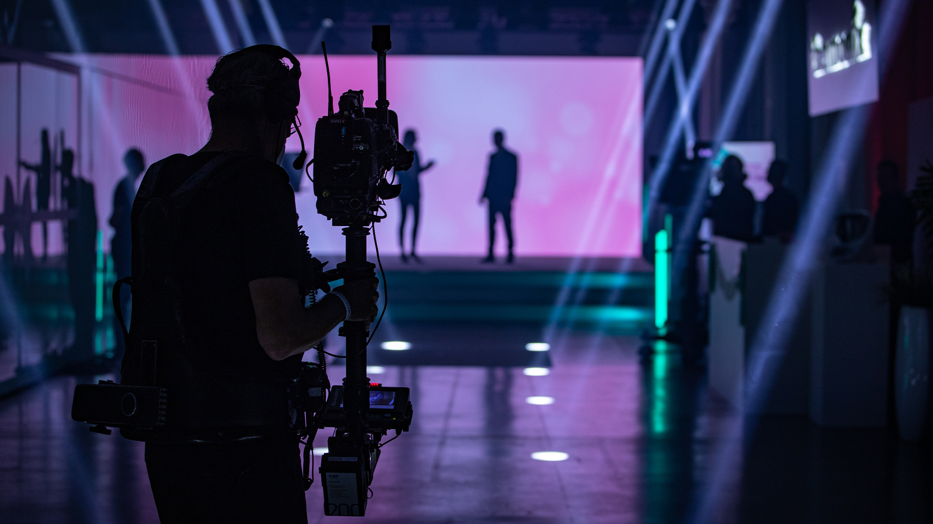 Silhouette eines Steadicam-Operators vor einer pink leuchtenden LED-Wand mit zwei Personen auf der Bühne