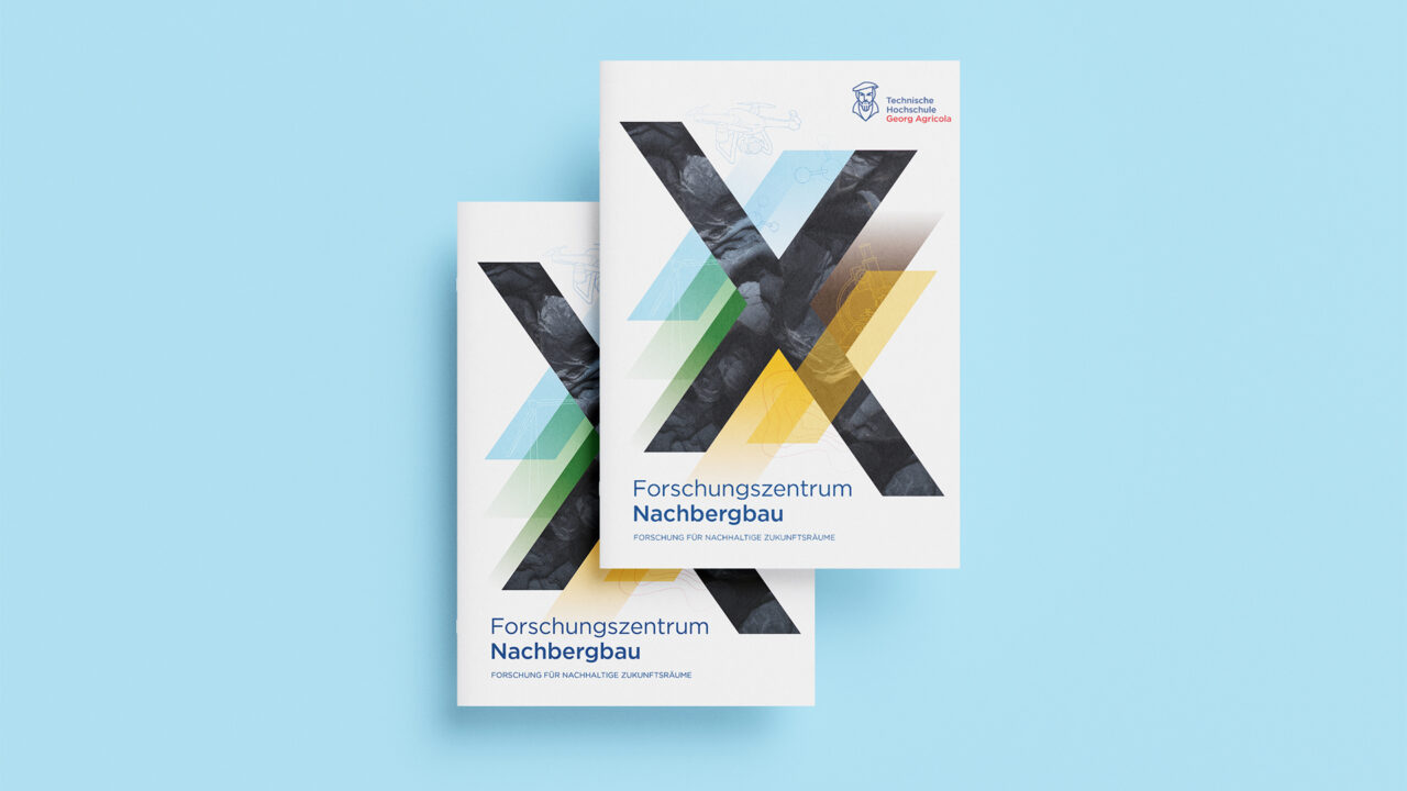 Zwei Exemplare der Jubiläumsbroschüre des Forschungszentrums Nachbergbau mit großem X aus Kohlestruktur und farbigen Bändern auf hellblauem Hintergrund